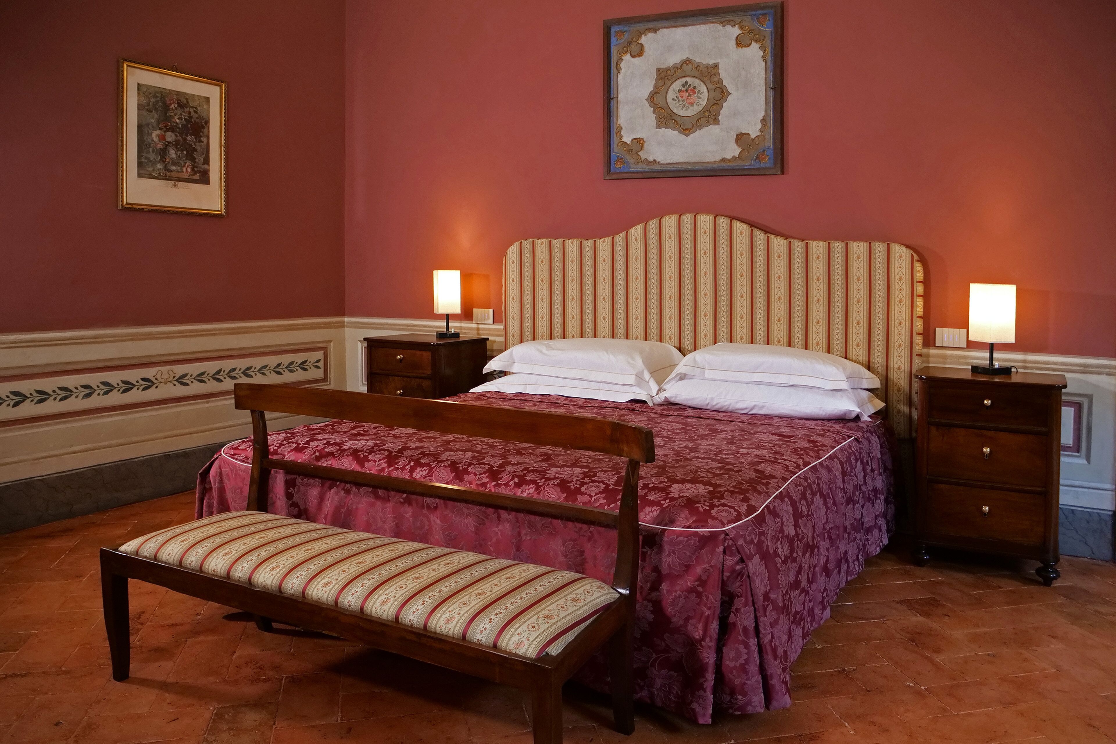 A bedroom with a large bed, a bench, two bedside tables, and a nightstand.