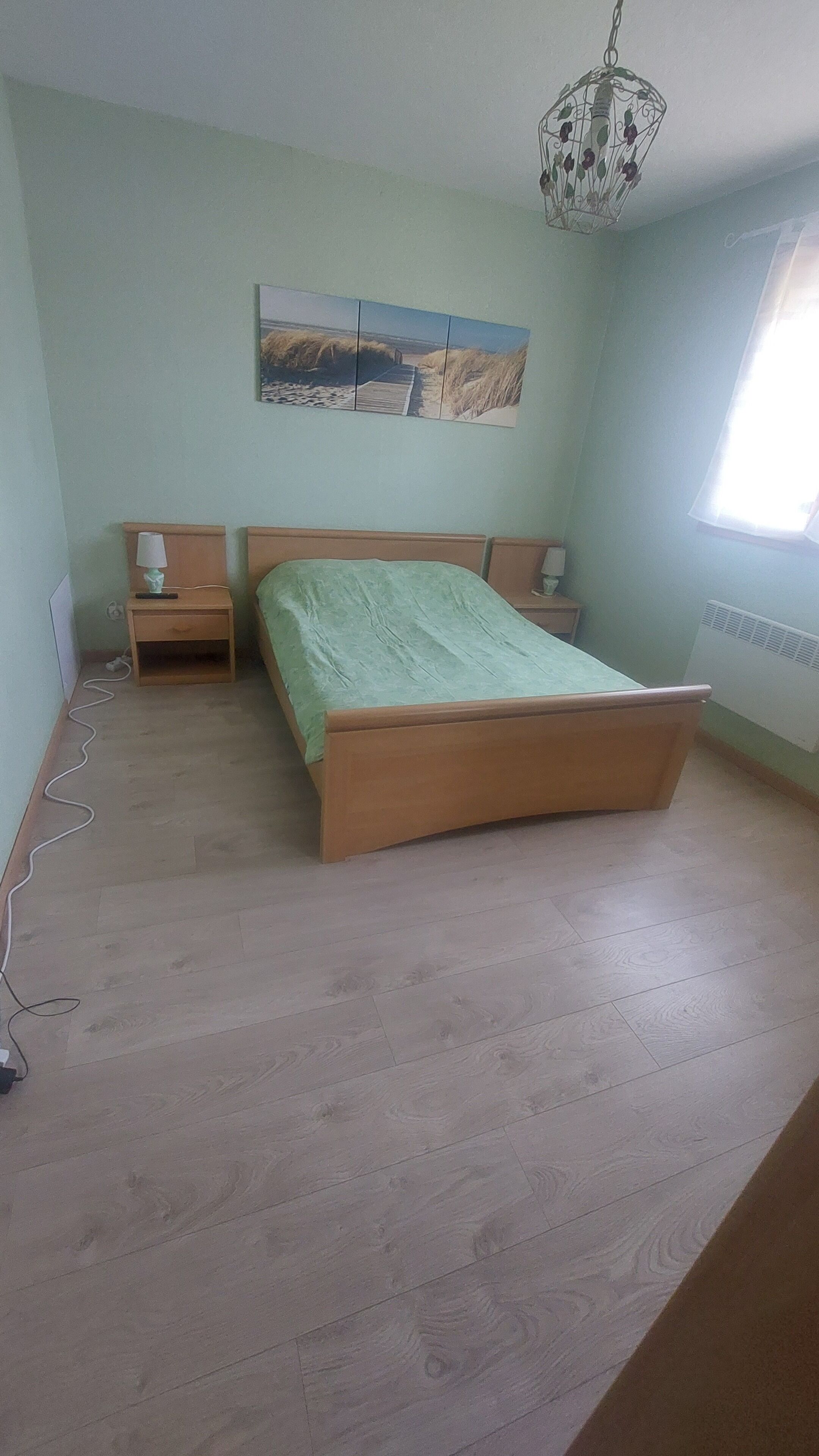 A bedroom with a wooden bed, a nightstand, a lamp, and a wall-mounted picture.