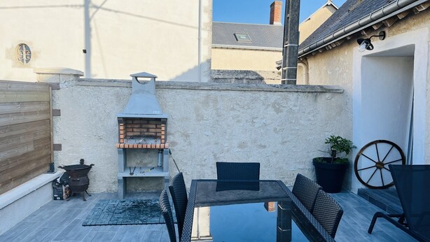 An outdoor patio with a glass table and wicker chairs, a brick pizza oven, and a potted plant.