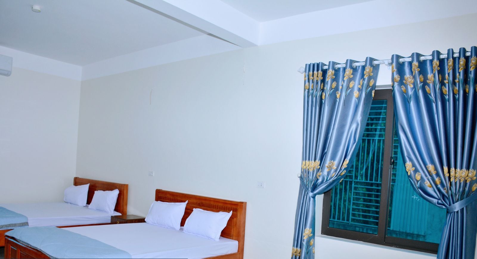Quarto de hotel com duas camas, uma janela com cortinas azuis e design moderno e limpo.