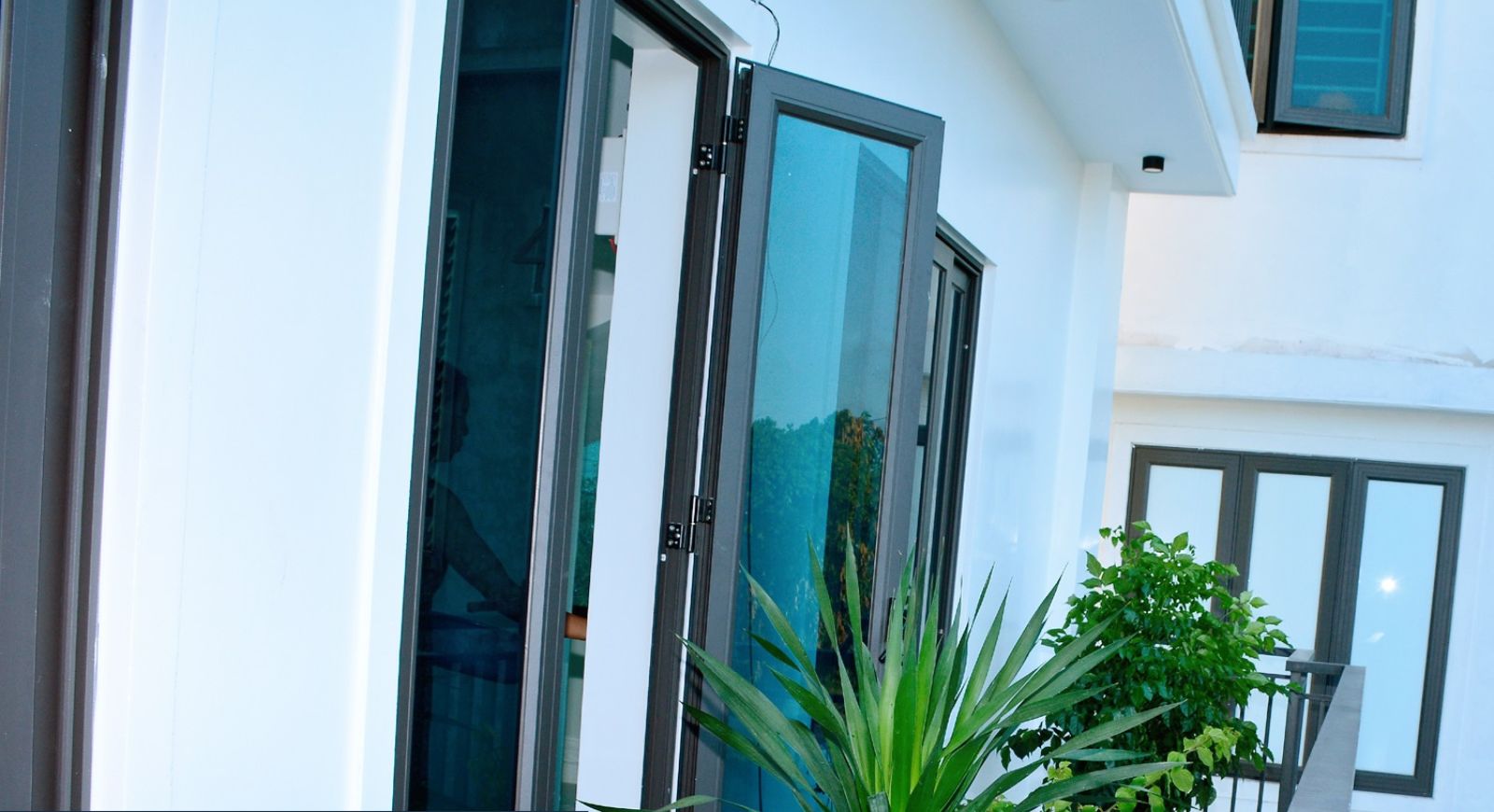 A modern building with large glass doors and windows, a balcony with potted plants, and a sign for VINH AIRPORT HOTEL.