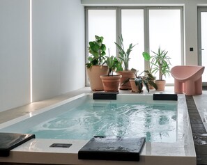 Zona d'una piscina interior moderna, amb una piscina rectangular, envoltada per jardineres de terracota amb diverses plantes, i una cadira rosa.