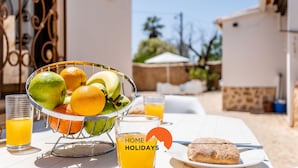 Una mesa de desayuno con un frutero, vasos de jugo de naranja y un plato de comida.