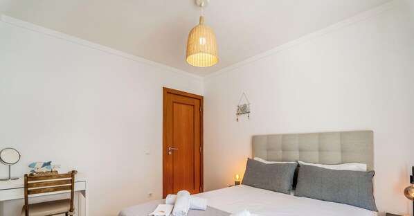 A bedroom with a bed, a wooden door, a bedside table with a lamp, and a hanging light fixture. - #172 Falésia Beach by Home Holidays (Albufeira)