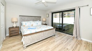 A bedroom with a bed, two bedside tables, a ceiling fan, a sliding glass door to a balcony, and a wooden floor. - Modern and Elegant condo just steps from Siesta Key Beach. Sleeps 6. (Sarasota)