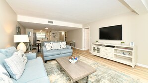 A living room with a sofa, coffee table, TV, and a kitchen area in the background. - Modern and Elegant condo just steps from Siesta Key Beach. Sleeps 6. (Sarasota)