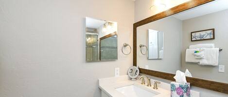A bathroom with a large mirror, two sinks, a towel rack, and a framed picture on the wall.