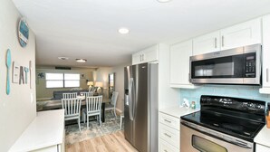 A modern kitchen with white cabinets, stainless steel appliances, and a dining area with a wooden table and chairs. - Modern and Elegant condo just steps from Siesta Key Beach. Sleeps 6. (Sarasota)