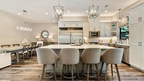 A modern kitchen with a central island, bar stools, pendant lights, and a dining area with a chandelier. - Luxury LAKEFRONT home  Insane view POPULAR spot 
Sleeps 16+ SERENITY (Kingsland)