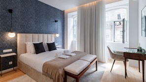 Ein modernes Schlafzimmer mit einem großen Bett, Nachttischen, einem Schreibtisch und Blick auf die Stadt.