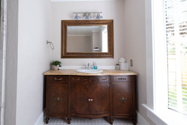 A bathroom with a wooden vanity, a large mirror, and a window with blinds.
