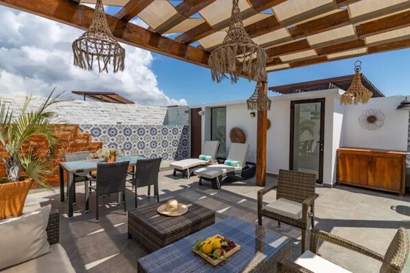 Une terrasse extérieure comprenant un espace repas, des chaises longues et un luminaire suspendu.