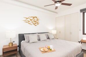 Une chambre bien rangée, avec un lit, des tables de chevet, un ventilateur de plafond et un élément décoratif mural.