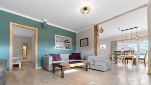 A spacious living area with a sofa, coffee table, and dining table. There is a bookshelf and a framed picture on the wall. - Zeit zu Zweit an der Wieke (Großefehn)