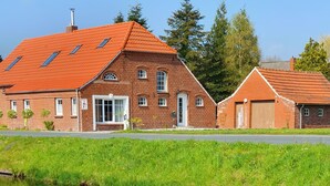 A traditional brick building with a red-tiled roof, a pond in the foreground, and yellow daffodils. - Zeit zu Zweit an der Wieke (Großefehn)