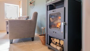 A cozy living room with a sofa, a fireplace, and a basket of firewood. - Zeit zu Zweit an der Wieke (Großefehn)