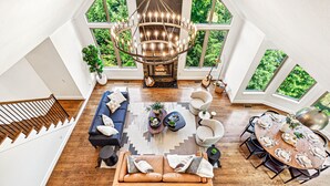 Um loft espaçoso com pé direito alto, lareira central, área de jantar e grandes janelas com vista para o verde.