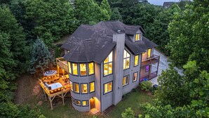 Uma casa de vários andares com varanda e terraço, cercada por vegetação densa.