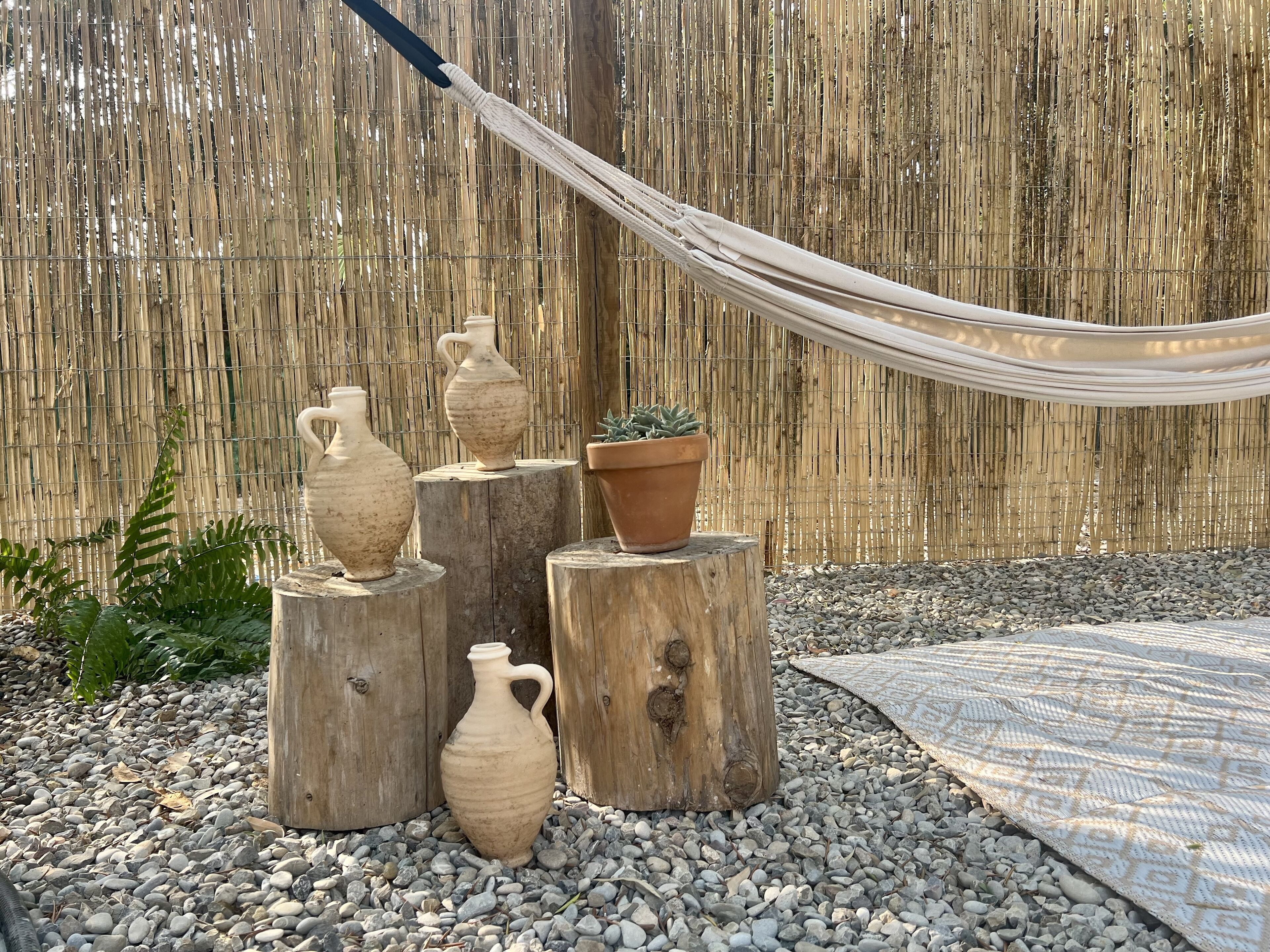 A hammock, three pottery vases, and a potted plant on wooden stumps in a garden setting.