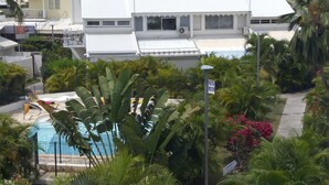 Une piscine entourée d’une végétation luxuriante et un bâtiment blanc doté d’un toit en métal.