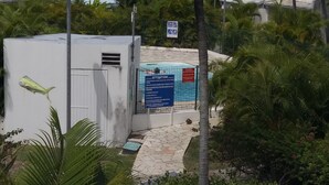 Un espace délimité par une clôture, avec un panneau indicateur, un petit bâtiment et une végétation luxuriante.