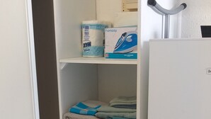Une armoire blanche avec plusieurs étagères, dont certaines contiennent des serviettes pliées et une boîte de lessive.