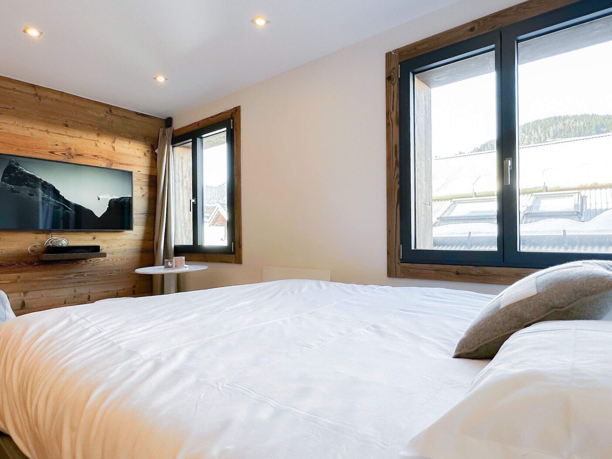 Ein Schlafzimmer mit einem großen Bett, einem an einer Holzwand montierten Fernseher und einem Fenster mit Blick auf eine verschneite Landschaft.