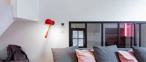 Un dormitorio moderno con una cama, almohadas, un taburete y una lámpara roja.