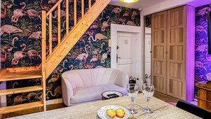 A room with a wooden staircase, a white sofa, a dining table with two wine glasses and a plate of cookies, and a door with a wooden wardrobe.