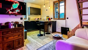A modern living room with a TV, wooden cabinets, a sofa, and a kitchen area with a window.