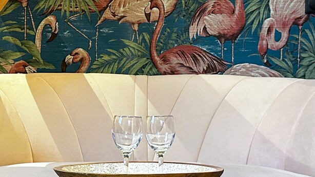A modern living room with a white sofa, a wooden coffee table with two glasses, and a tropical-themed mural in the background.