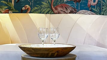 Een moderne woonkamer met een witte bank, een houten salontafel met twee glazen, en een tropische muurschildering op de achtergrond.