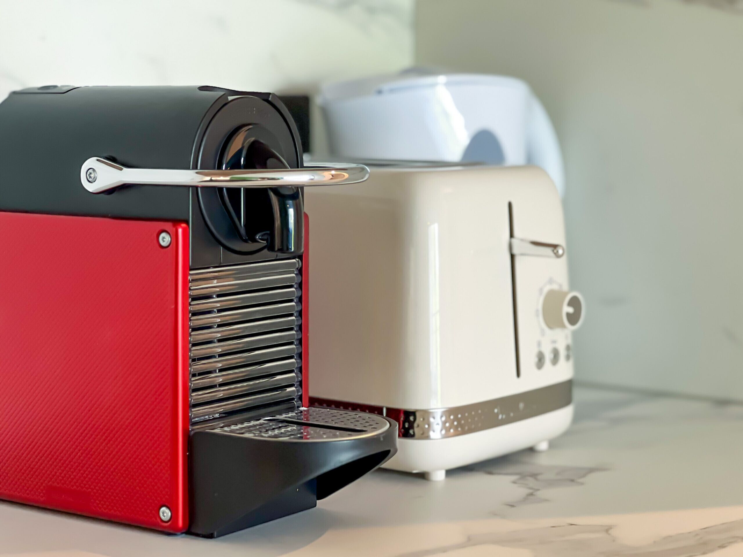A red and black coffee machine with a silver water reservoir and a white toaster with a control panel.