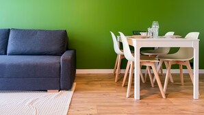 Uma sala de estar moderna com um sofá cinza escuro, uma mesa de jantar branca com cadeiras e uma parede verde.