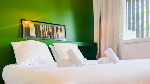 Cama bem arrumada com lençóis e almofadas brancos, parede verde e quadro na parede acima da cama.