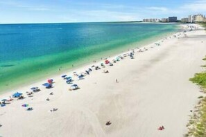 A beach with rows of umbrellas and beach chairs, a clear blue sea, and buildings in the background. - Marco Island Getaway! Quick Walk to the Beach! (Marco island)