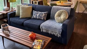 Ein gemütliches Wohnzimmer mit einem dunkelblauen Sofa, einem Holztisch und einem Essbereich im Hintergrund.