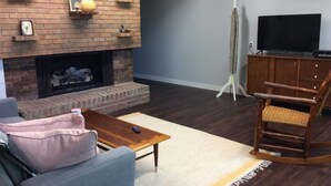 Ein Wohnzimmer mit Kamin, Fernseher, Schaukelstuhl und Sofa.