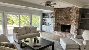 A modern living room with a fireplace, a sofa, a coffee table, and a bookshelf. - Secluded Home w/pool located 5 mins from American River  (Carmichael)