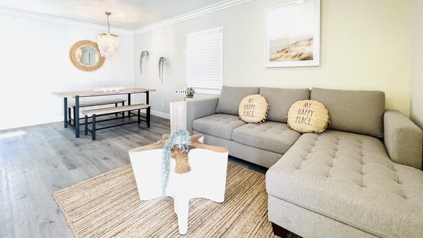 A living room with a grey sofa, a round table with benches, a white coffee table, and a wall-mounted mirror.