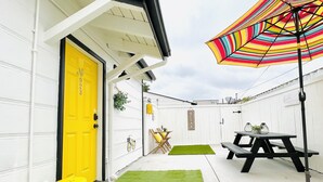 A white building with a bright yellow door, a picnic table, and a colorful umbrella.