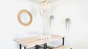 A minimalist dining area with a wooden table and bench, a woven mirror, and decorative plants.
