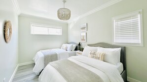 A bedroom with two beds, a chandelier, a window with blinds, and wall art.