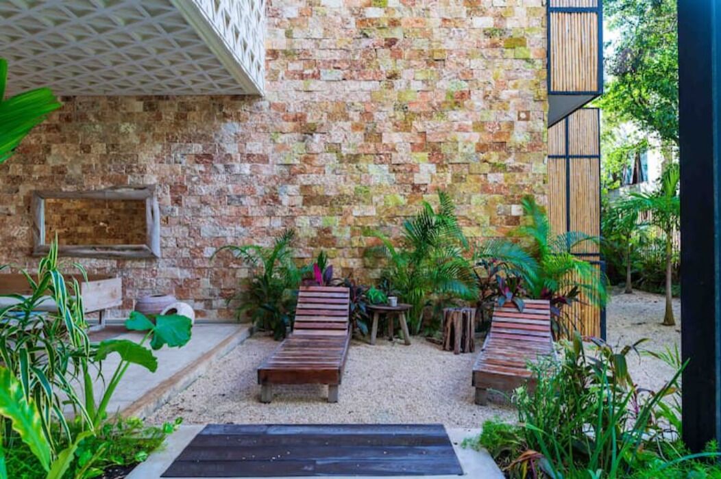 A patio area with wooden loungers, a brick wall, and various plants.