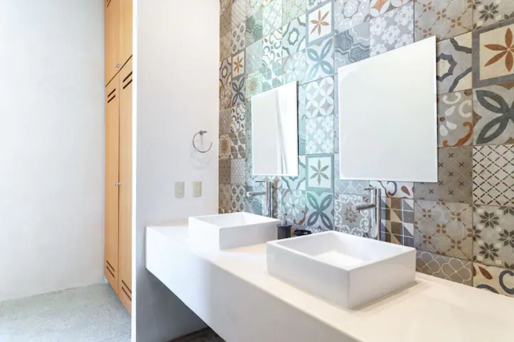 Un baño moderno con dos lavamanos blancos, un espejo y un salpicadero de azulejos.
