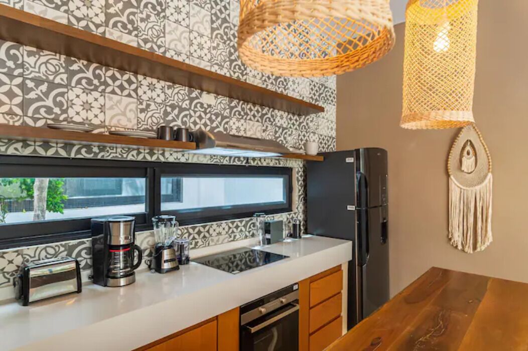 A modern kitchen with a patterned backsplash, a built-in oven, a refrigerator, and a wooden dining table.