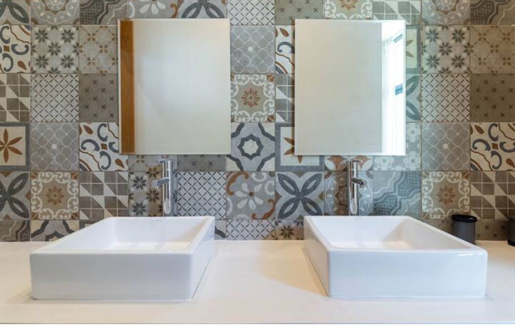 A bathroom with two white sinks and a mirror above each. The wall is decorated with patterned tiles.