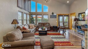 A cabin with a living room featuring a sofa set, a coffee table, and a patterned rug. There is a chandelier, a fireplace, and a bookshelf with books.