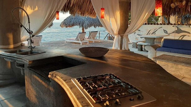 A beachside lounge with a gas stove, white curtains, and a thatched roof. - Villa Kassondra del Mar (Acajutla)