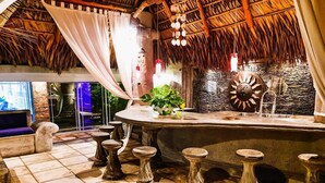 A bar area with a stone counter, stools, and a decorative wall. - Villa Kassondra del Mar (Acajutla)